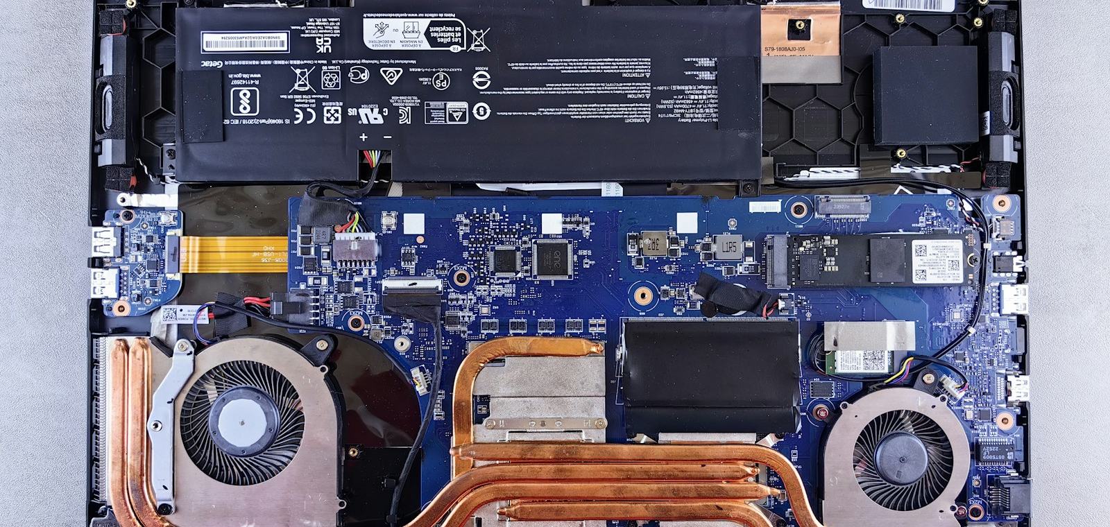 A laptop opened up on a bench with the battery, cooling fans and heat pipes exposed.