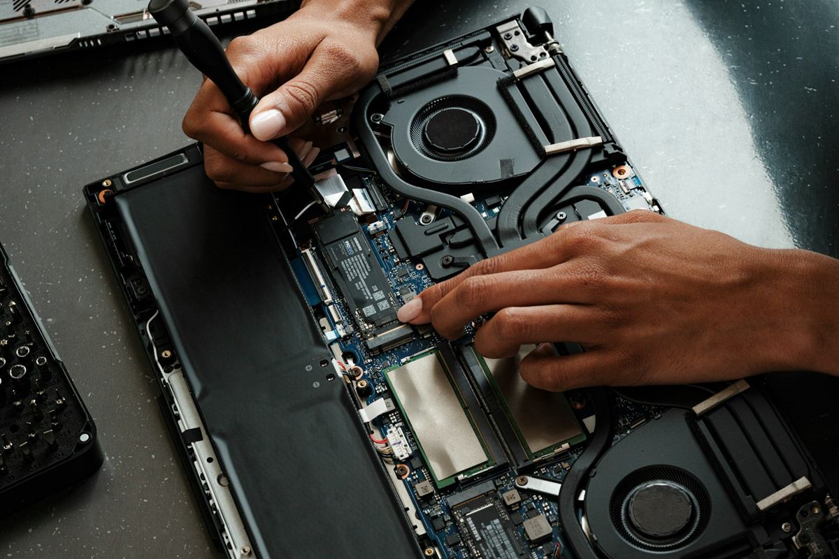 An engineer's hands using a precision screwdriver inside an open laptop at a table.